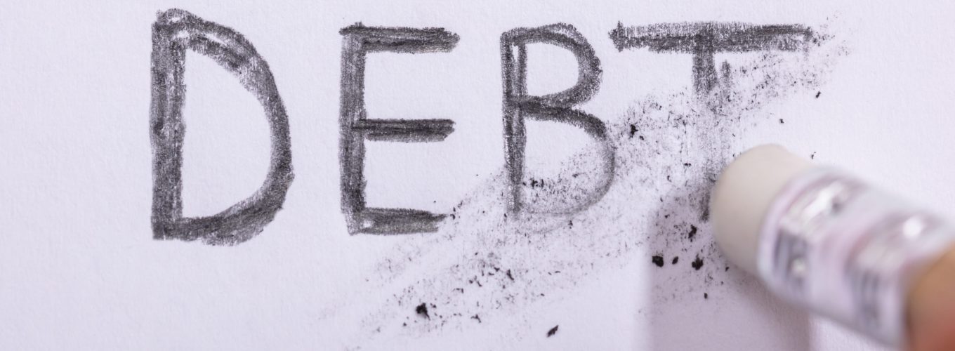 Close-up Of Pencil Eraser Erasing Debt Word On White Paper