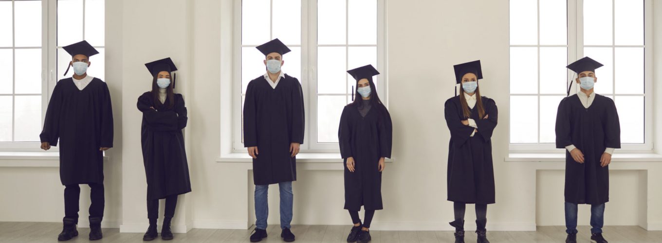 Graduation from university during pandemic concept. Group of multiracial students university graduates in protective medical face masks and mantles standing and keeping social distance indoors